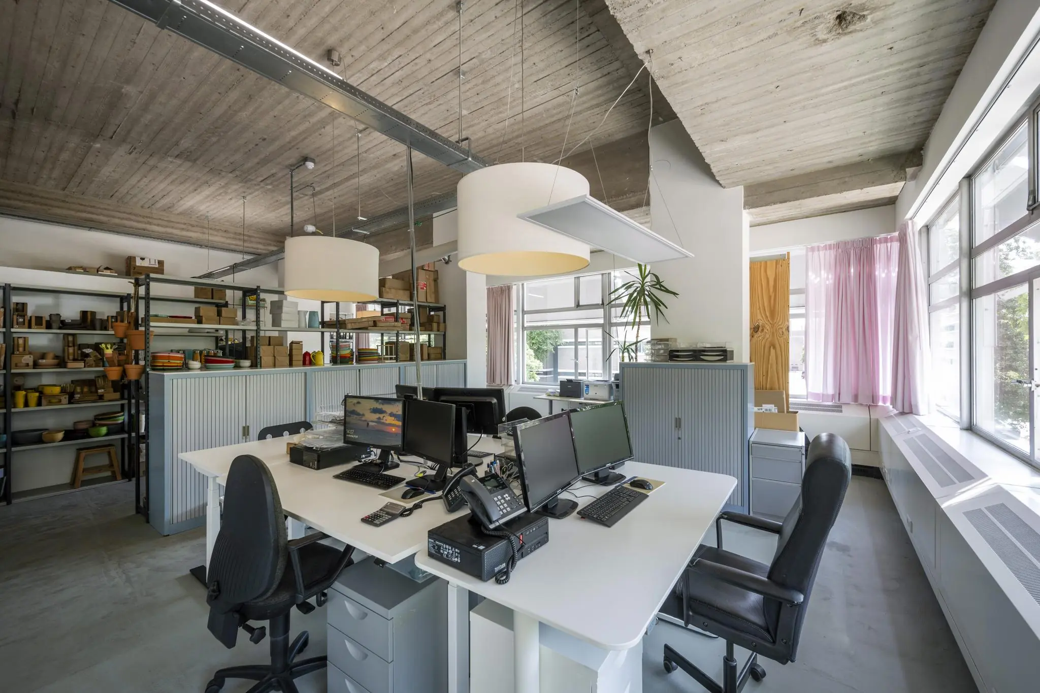 Modern kantoorinterieur aan de Van Leijenberghlaan met gedeelde werkplekken, computers en open stellingkasten vol servies.